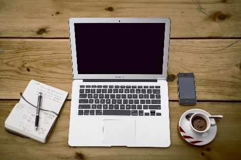 A picture containing a laptop, a cellphone, a notepad, and a cup of coffee on the table