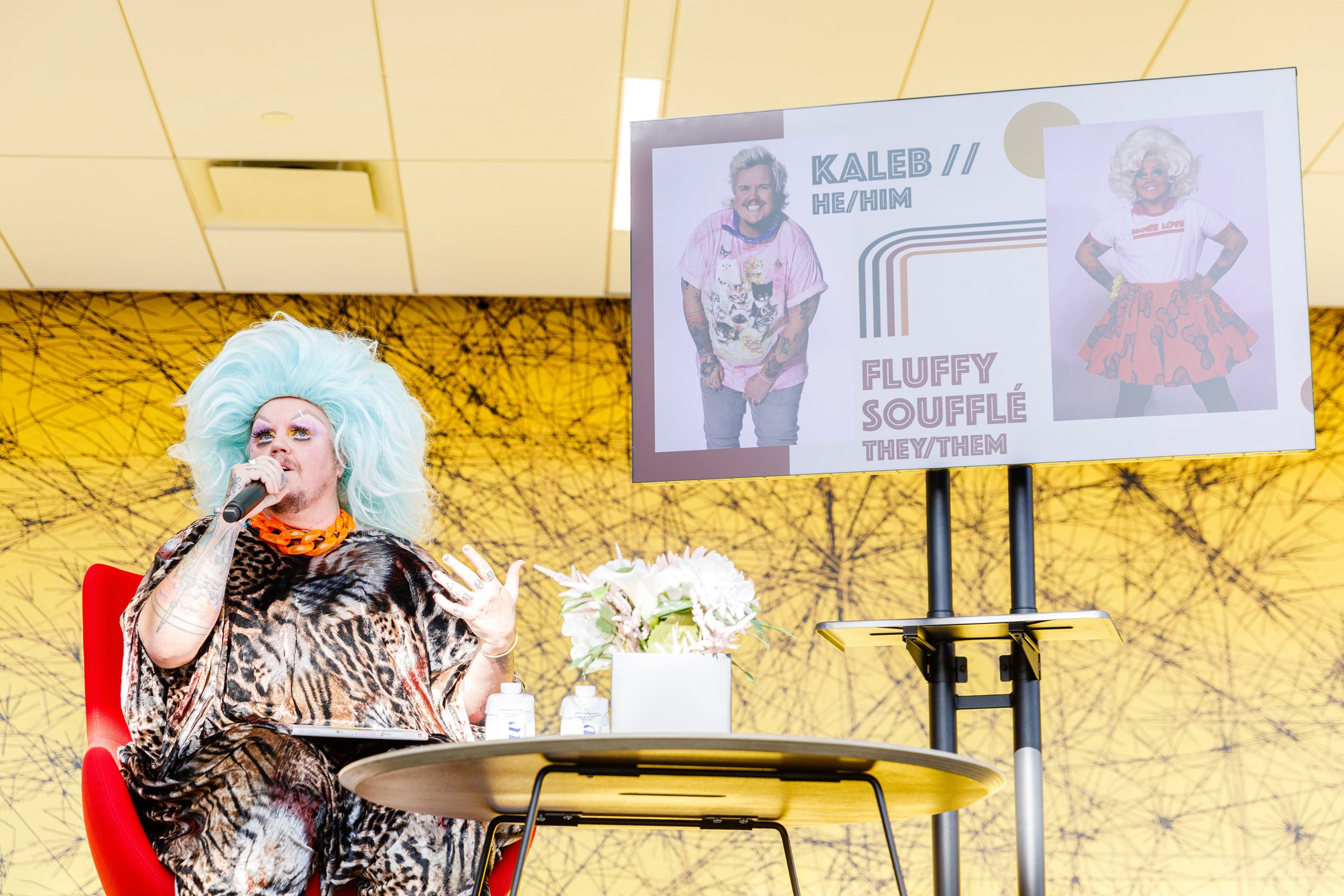 drag queen Fluffy Souffle sitting on a chair onstage for a presentation