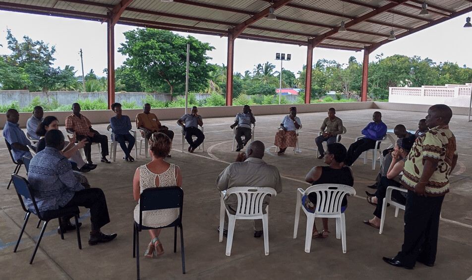 The workshop participants and facilitators sitting in the gymnasium, an outdoor open-air room