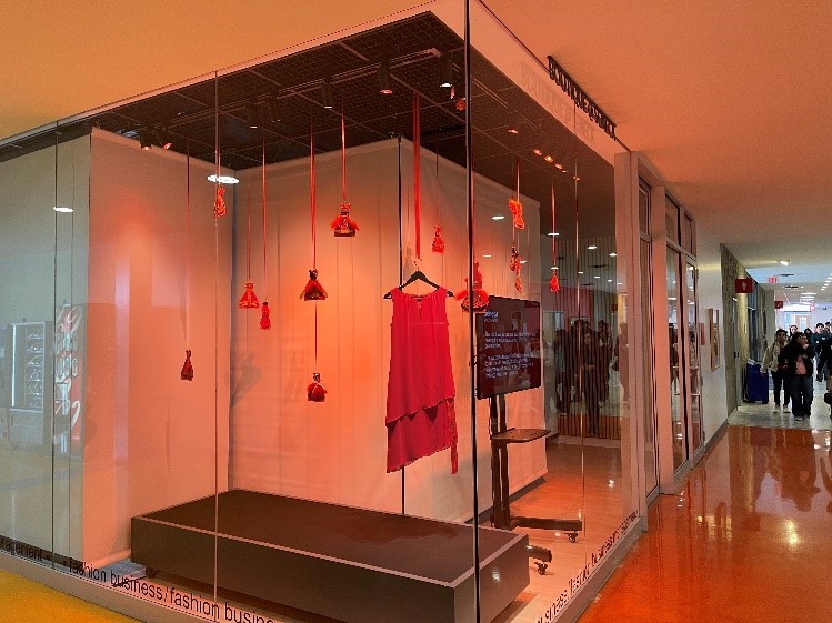 A display case with a hanging red dress surrounded by hanging paper dresses