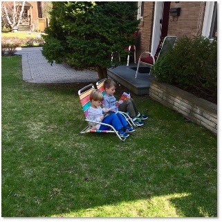 Two young children reading books in the sun on a front lawn